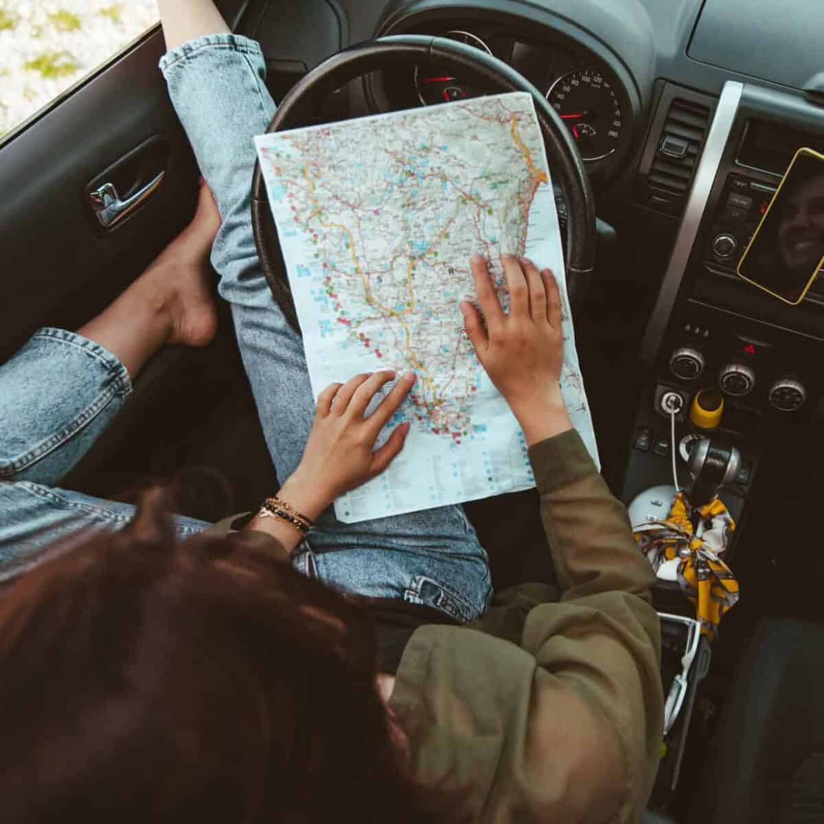 Woman sitting in the driver's seat of a car looking at a paper map.